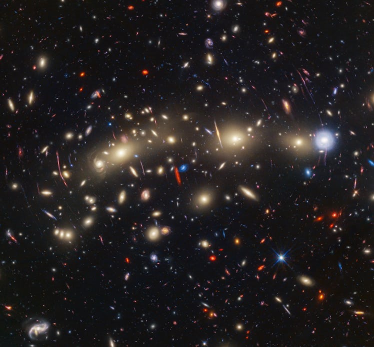A field of galaxies on the black background of space. In the middle is a collection of dozens of yel...