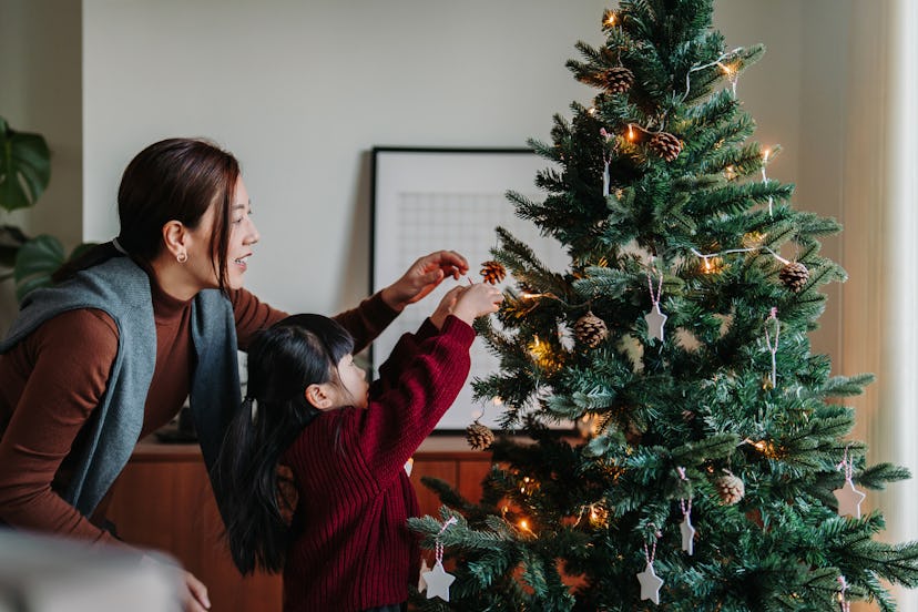 single mother daughter decorating Christmas tree at home together. 