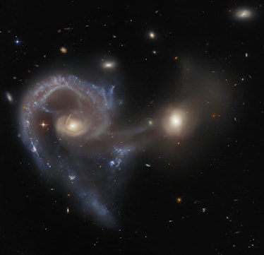 photo of two galaxies with streams of gas and dust between them, with smaller galaxies in the backgr...