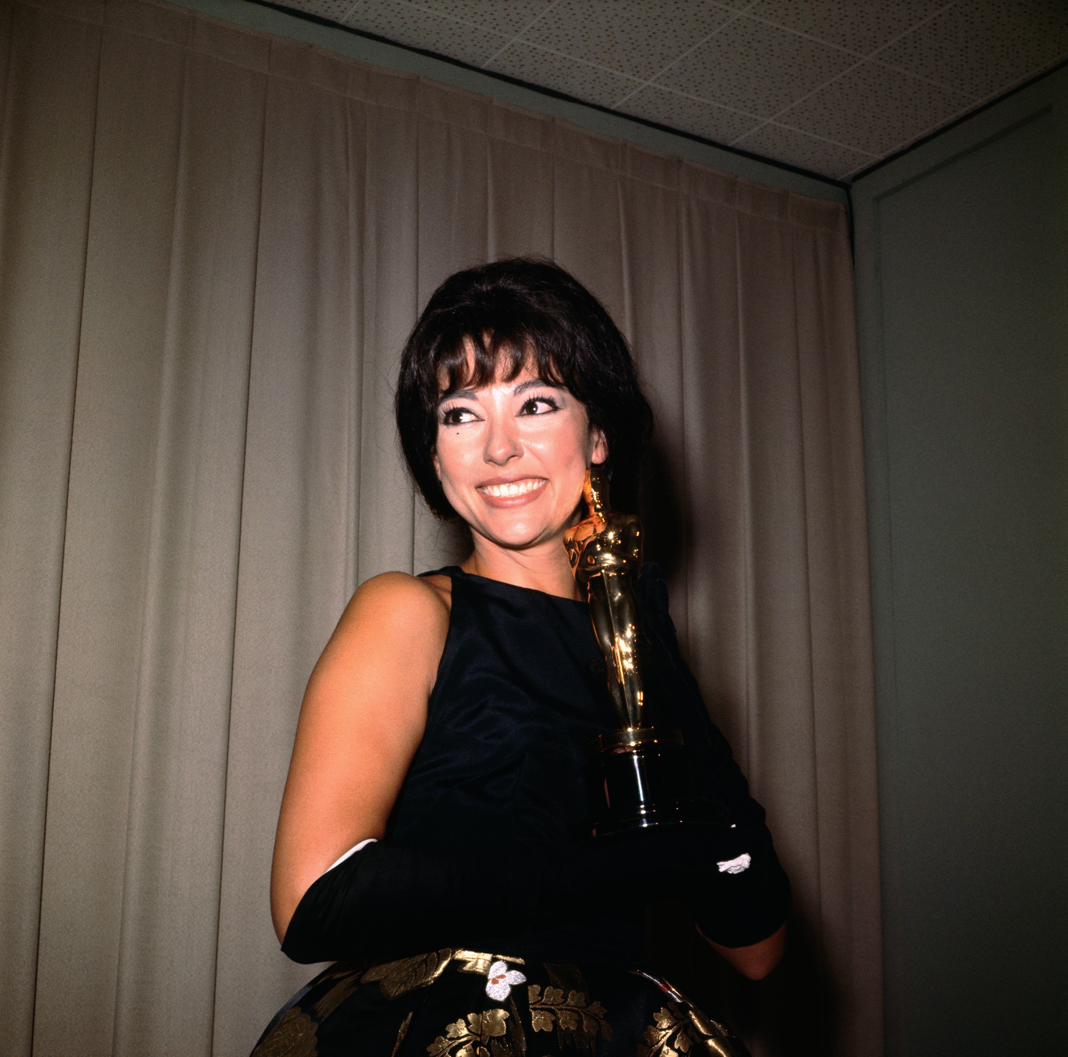 Actress Rita Moreno smiling as she holds her Academy Award.