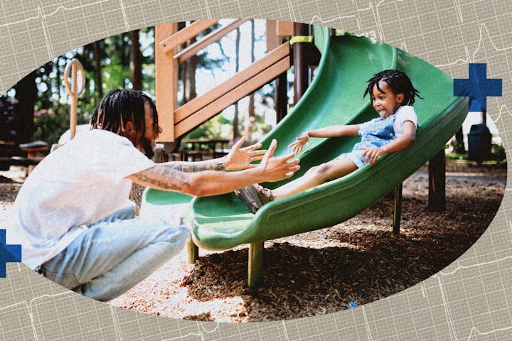 A child going down a slide at a playground, into their dad's arms.