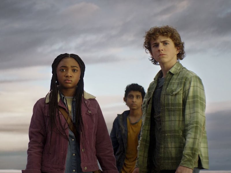 Three teenagers stand together with serious expressions against a cloudy twilight sky.