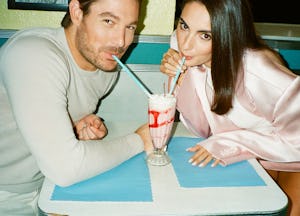 Two people smiling while sharing a milkshake with two straws at a diner table with a blue and white ...