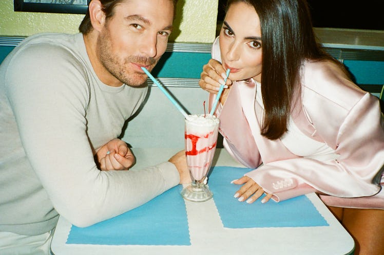 Two people smiling while sharing a milkshake with two straws at a diner table with a blue and white ...