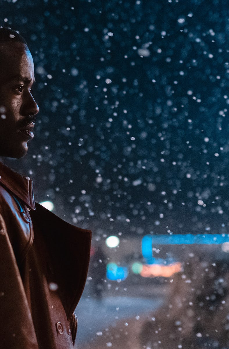 Man in red jacket looking contemplative at night with illuminated snowflakes falling around him.