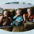 Three children sitting on a couch, eating pizza and watching TV,