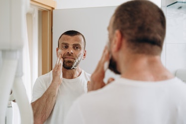 A man applying minoxidil to his beard in a bathroom mirror.