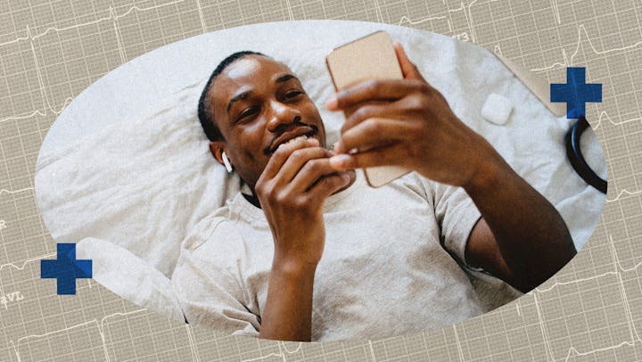 A man lying on his bed, looking at his cell phone.
