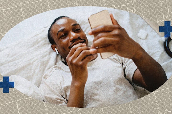 A man lying on his bed, looking at his cell phone.