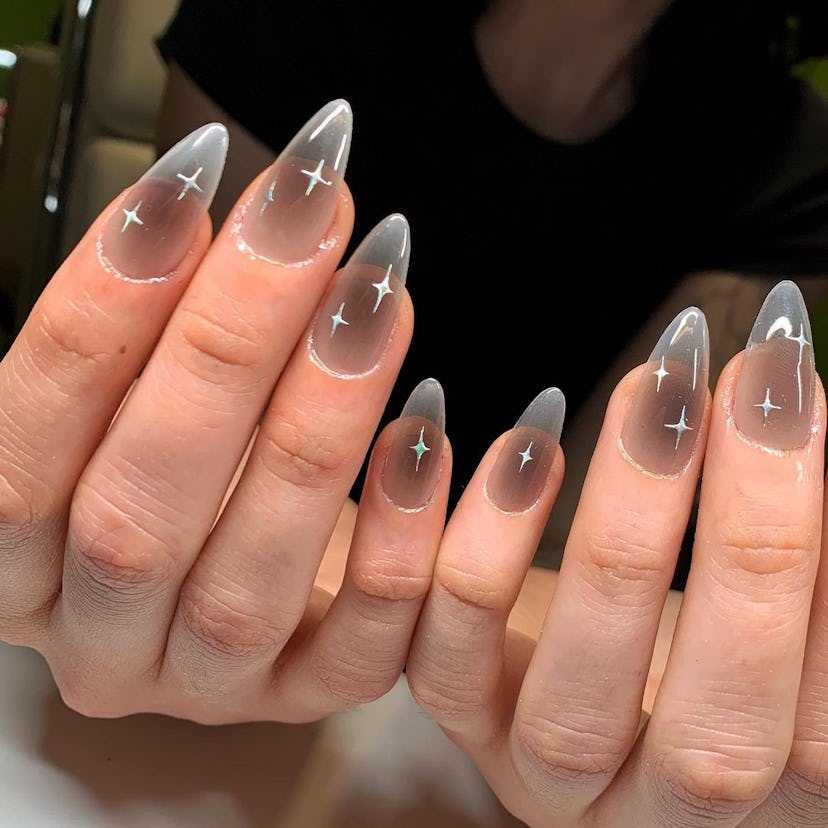 Sheer grey polish with celestial stars are an on-trend Capricorn nail design for 2024.