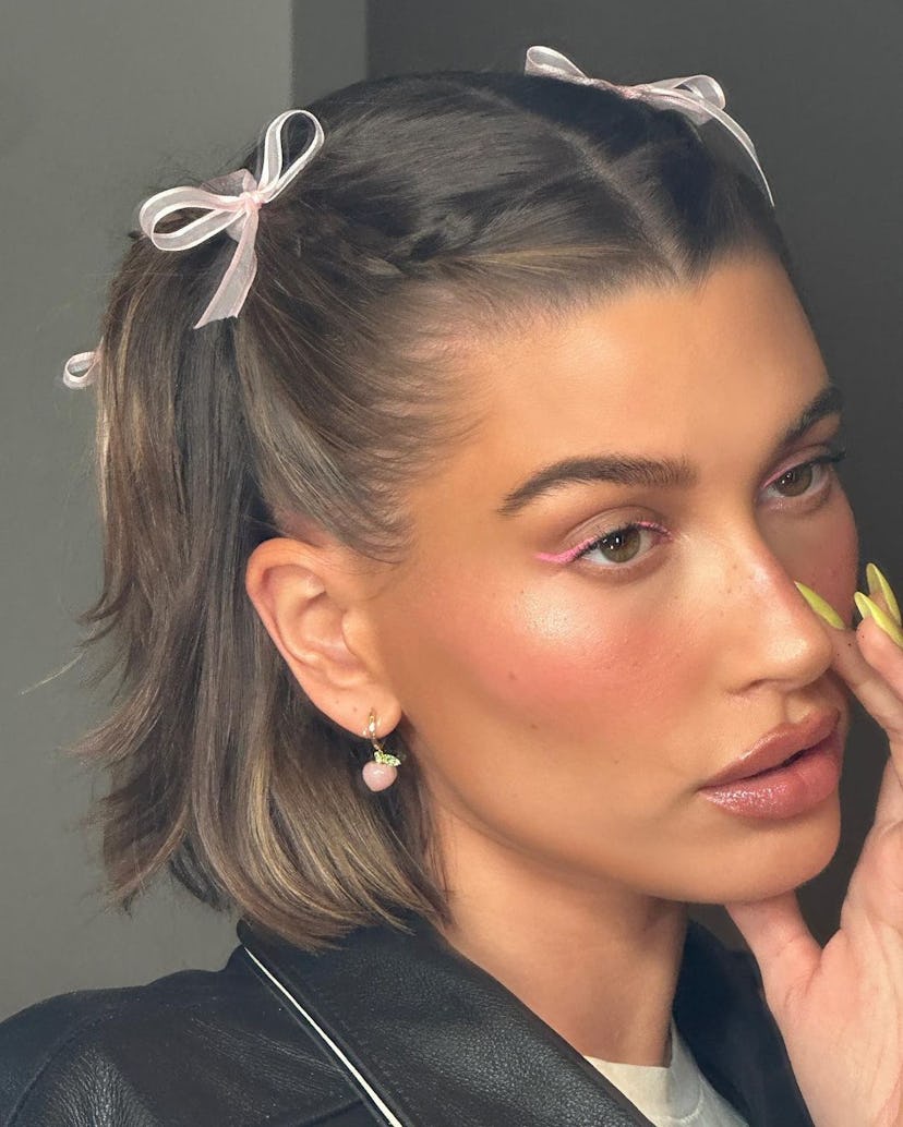 Hailey Bieber is a fan of coquette balletcore ribbons, and was spotted with tiny pink bows in her ha...