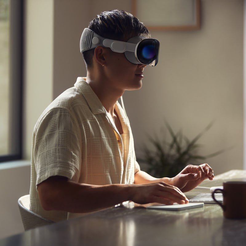 A person wearing Apple Vision Pro while using a Magic Keyboard and Magic Trackpad