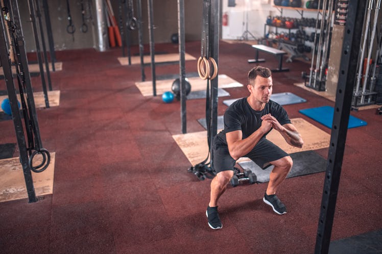 A man doing squats a gym for an EMOM workout.