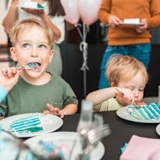 Two little boys eat cake at a birthday party. 