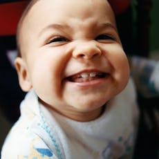 An infant smiles, showing off their new teeth. 