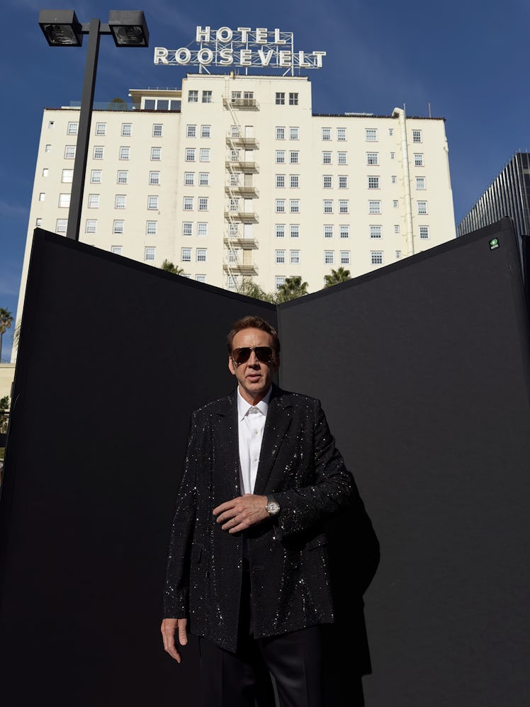 Nicolas Cage wears a black glitter blazer, white button down shirt, sunglasses, watch and black pant...