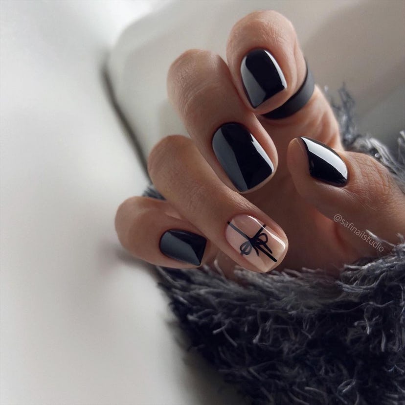 Glossy black nails with bow nail art on an accent nail are a festive holiday nail design for 2023.