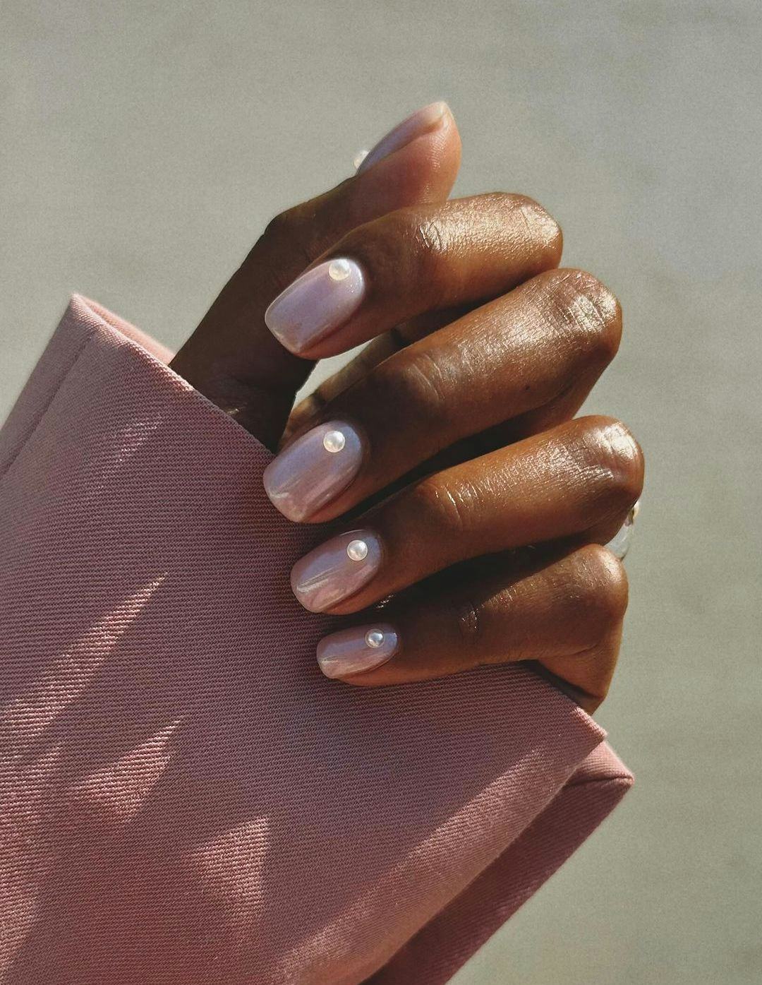 A light pink minimal nail design with 3D pearls is a classy manicure idea for 2023 holiday nails.