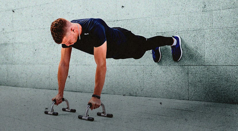 A man doing push-ups with his hands on elevated bars on the ground and feet against a wall.