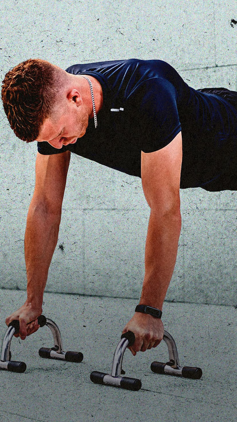 A man doing push-ups with his hands on elevated bars on the ground and feet against a wall.