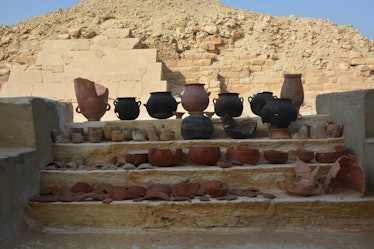 Clay pots and jars sit on a step with a pyramid in the background