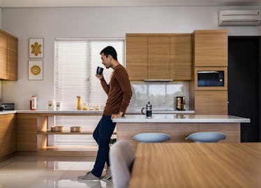 Man leaning against table and drinking coffee alone in kitchen
