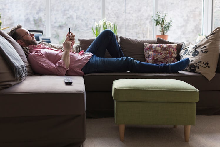 Man lying on couch alone staring at phone
