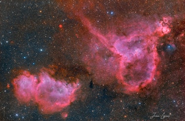 Color photo of two nebulae in shades of red, purple, and pink; the one on the right is an upside dow...
