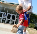 孩子背着背包在学校外面拖着他爸爸试图控制他。