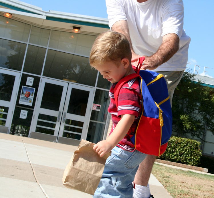 Young child wearing backpacking outside of school pulling away while his dad tries to control him.