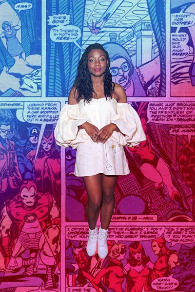 Indie auteur Nia Dacosta in a white dress and white boots with a comic book page collage in the back...