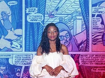 Indie auteur Nia Dacosta in a white dress and white boots with a comic book page collage in the back...