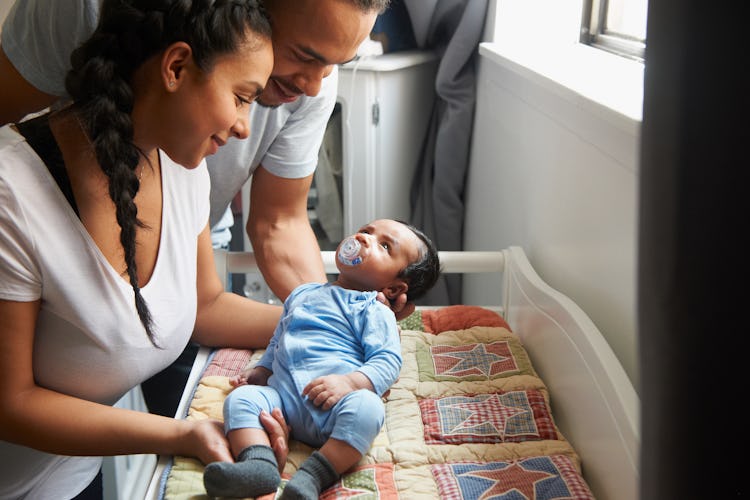 A mom and dad put their baby down to sleep in a crib.