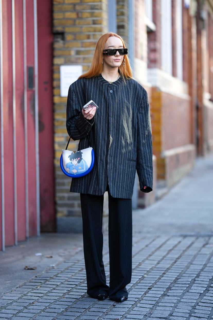 A guest wears black sunglasses, a black striped print pattern oversized jacket, a white shiny leathe...