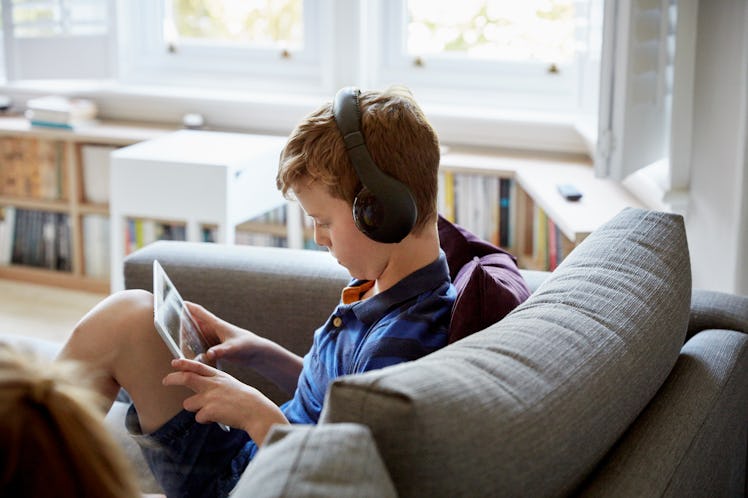 A child sitting on a couch, using a tablet while wearing headphones.