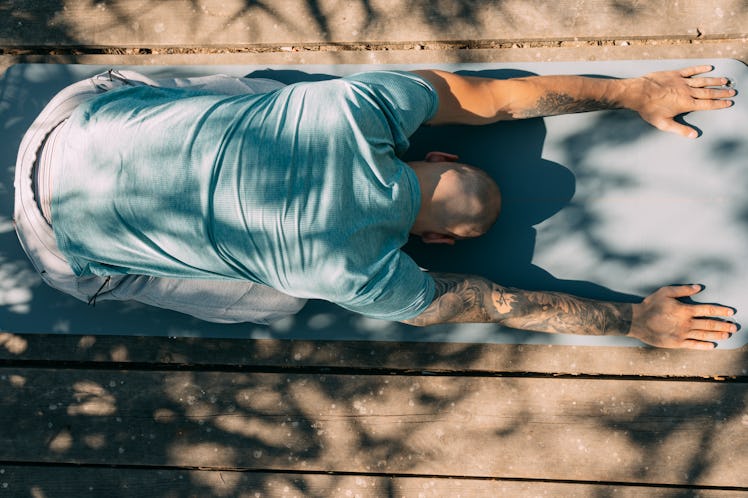 A man in child's pose on a yoga mat.