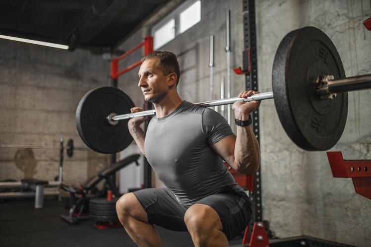 A man in a gym doing barbell squats.
