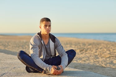 A man doing a butterfly stretch outside by a beach.