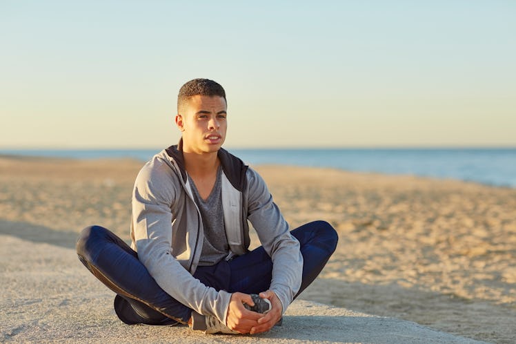 A man doing a butterfly stretch outside by a beach.