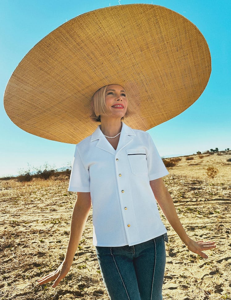 Michelle Williams wears a pearl necklace, white shirt, straw hat and denim jeans.