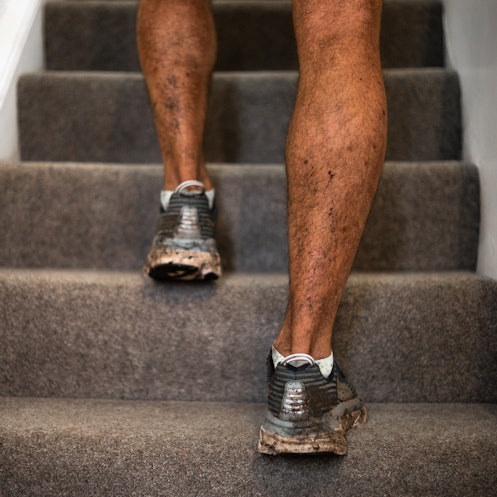 Close up of the calves of a man in sneakers climbing carpeted steps at home.