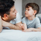 A dad and son on a bed, talking together.