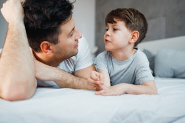 A dad and son on a bed, talking together.