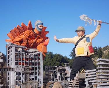 two men wearing costumes posing above a fake cityscape