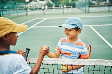 Two kids shake hands over a tennis net.