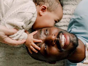 A dad and his baby lying on a beige rug