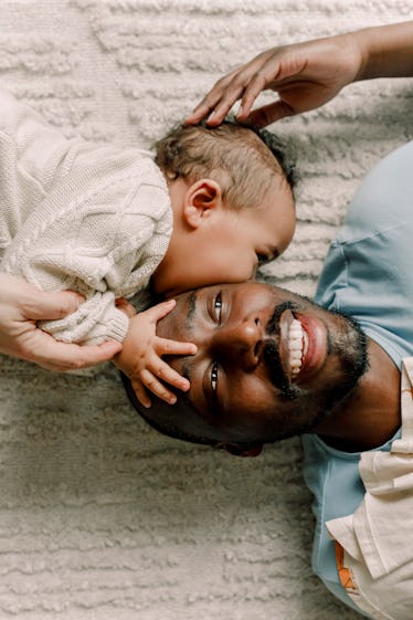 A dad and his baby lying on a beige rug 