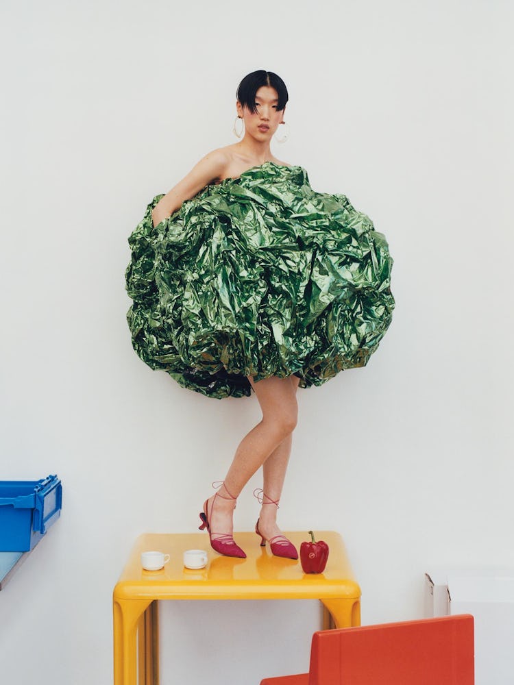 Model wears a green gown, gold hoop earrings and red shoes.