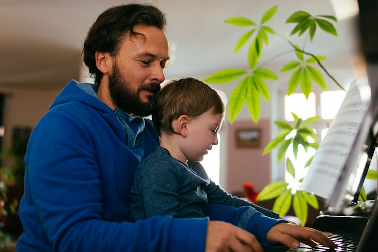 Son sitting on father's lap as they play the piano together