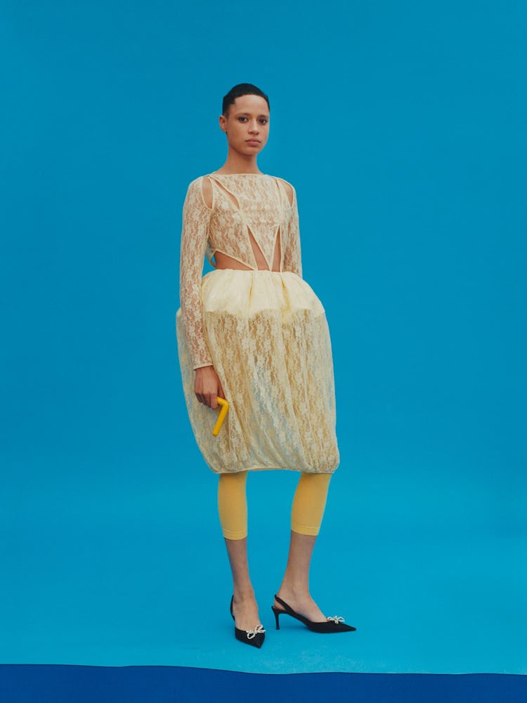 Model wears yellow laced dress with yellow tights, and shoes.